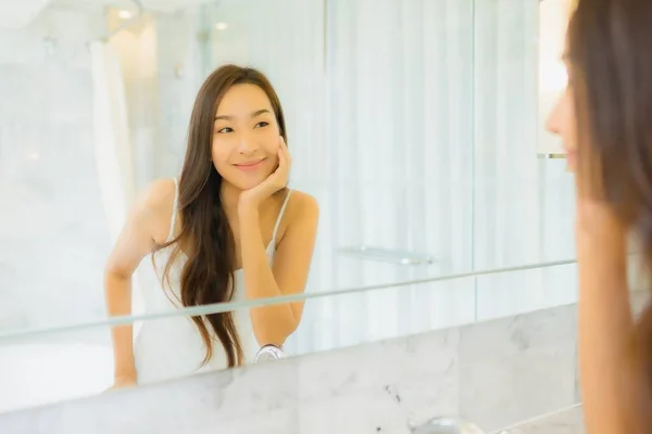 ポートレート美しいです若いですアジアの女性チェックアップと作ります彼女の顔上のミラーでバスルーム内装 — ストック写真
