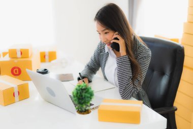 Güzel Asyalı iş kadını portresi evden bilgisayarlı cep telefonuyla karton kutuyla çevrimiçi alışveriş için hazır bekliyor.