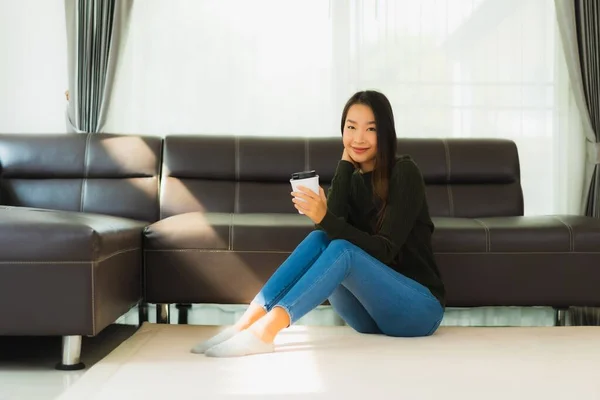 肖像画美しい若いアジアの女性はリビングルームのインテリアでソファとコーヒーカップとスマート携帯電話を使用します — ストック写真
