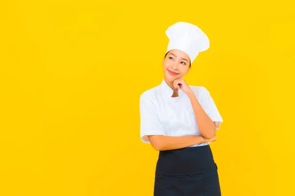 肖像画美しいです若いアジア人女性でシェフまたは調理制服とともに帽子で黄色隔離された背景 — ストック写真