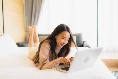 Yatak odasının iç kısmında dizüstü bilgisayar kullanan güzel Asyalı kadın portresi.
