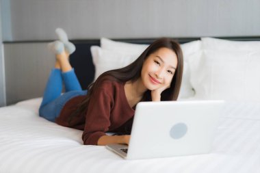 Güzel bir Asyalı kadın yatak odasının iç kısmında bilgisayar kullanıyor.