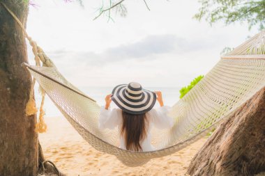 Güzel bir Asyalı kadın portresi deniz kıyısındaki hamakta dinleniyor.