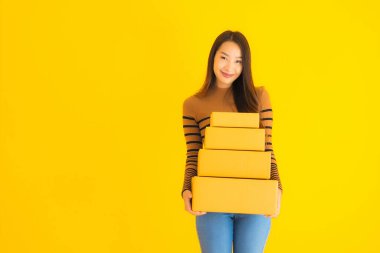 Sarıya boyanmış arka planda elinde karton kutu tutan güzel Asyalı bir kadın.