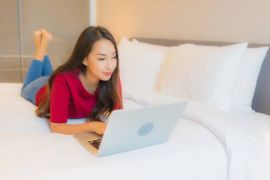 Güzel bir Asyalı kadın yatak odasının içinde dizüstü bilgisayar kullanıyor.