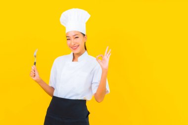 Güzel bir portre genç Asyalı kadın aşçı ya da aşçı üniforması giyiyor sarı izole arka planda çatal ve kaşıkla.