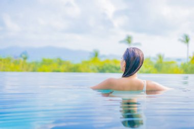 Güzel bir Asyalı kadın portresi gezide deniz manzaralı açık havuzda yüzüyor.