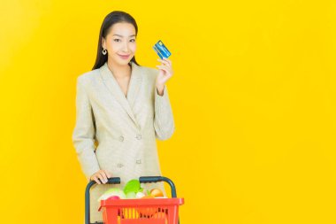 Renkli arka planda süpermarketten alınmış market sepetiyle gülümseyen güzel Asyalı kadın portresi.