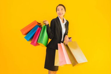 Sarı izole edilmiş arka planda alışveriş merkezinden alışveriş çantasıyla güzel bir genç Asyalı kadın portresi.