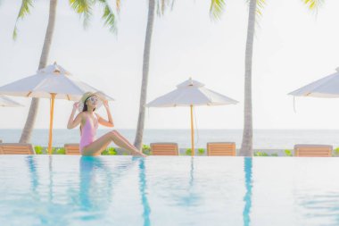 Güzel bir Asyalı kadın portresi. Tatil gezisinde deniz manzaralı açık havuz etrafında rahatça yüzebiliyor.