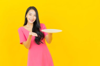 Asyalı güzel bir kadının portresi. Sarı arka planda boş tabak tabağıyla gülümsüyor.