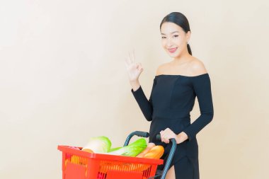 Renkli arka planda süpermarketten alınmış market sepetiyle gülümseyen güzel Asyalı kadın portresi.