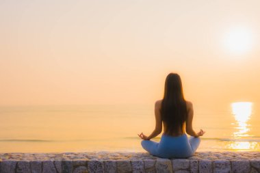 Genç Asyalı kadının portresi sağlık için gün doğumunda deniz kıyısı okyanusunda meditasyon yapıyor.