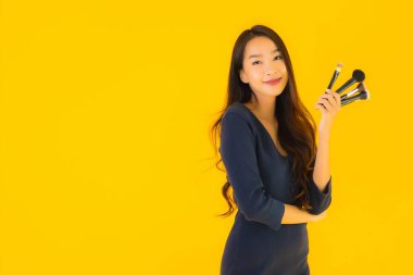 Sarı izole arkaplanda makyaj fırçası olan güzel bir Asyalı kadın portresi.