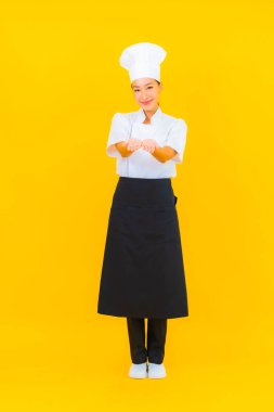 Güzel bir Asyalı kadın portresi ya da sarı izole arkaplanda şapkası olan aşçı üniforması.