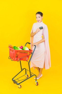Sarı arka planda süpermarketten alınmış sepetli güzel Asyalı kadın portresi.