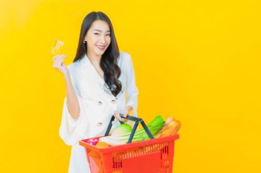 Renkli arka planda süpermarketten alınmış market sepetiyle gülümseyen güzel Asyalı kadın portresi.