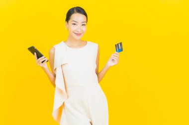 Asyalı güzel bir kadının portresi. Sarı arka planda kredi kartıyla gülümsüyor.