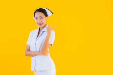 Güzel Asyalı genç Taylandlı hemşirenin portresi klinikteki ve hastanedeki hastalar için sarı izole edilmiş arka planda birçok eylem çalışmasında yer alıyor.