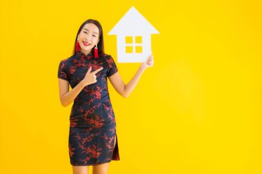 Güzel bir Asyalı kadın portresi, Çin elbisesi giyiyor. Sarı izole arka planda ev işareti var.