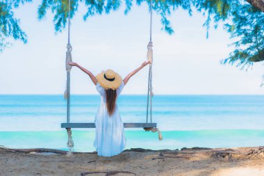 Güzel bir Asyalı kadın portresi gevşe, gülümse, deniz kıyısında sallan, mavi gökyüzü beyaz bulutuyla.