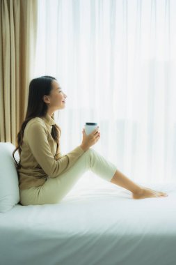 Yatak odasının iç tarafında, kahve fincanı olan Asyalı genç bir kadın.