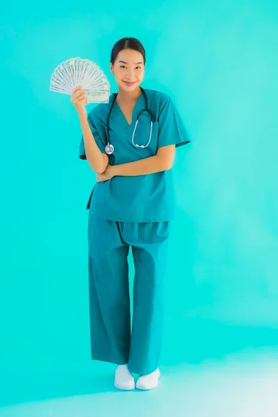 Portrait beautiful young asian doctor woman show money and cash on blue isolated background