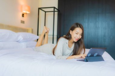 Güzel bir Asyalı kadının portresi yatak odasının içinde kredi kartıyla tablet kullanıyor.