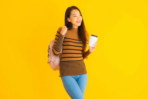 ポートレート美しいです若いですアジアの女性とともにBagpackとコーヒーカップ上の彼女の手で黄色隔離された背景 — ストック写真