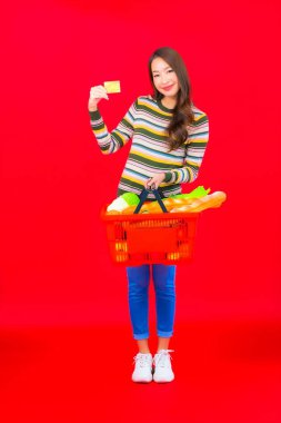 Marketten aldığı alışveriş sepetiyle kırmızı izole arka planda güzel bir Asyalı kadın portresi.