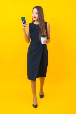 Kahve fincanı ve sarı arka planda akıllı cep telefonlu güzel Asyalı iş kadını portresi.