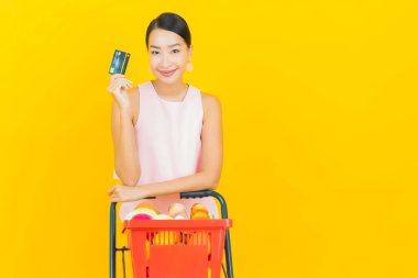 Asyalı güzel bir kadının portresi. Sarı arka planda süpermarketten alınmış alışveriş sepetiyle gülümsüyor.