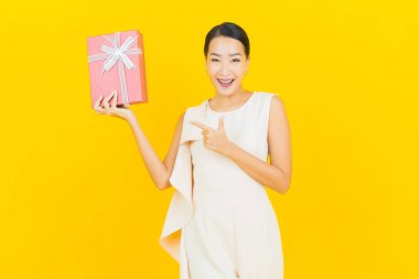 Asyalı güzel bir kadının portresi. Sarı arka planda kırmızı hediye kutusuyla gülümsüyor.