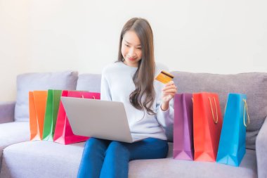 Güzel bir Asyalı kadının portresi evde online alışveriş için dizüstü bilgisayar kartı kullanıyor.