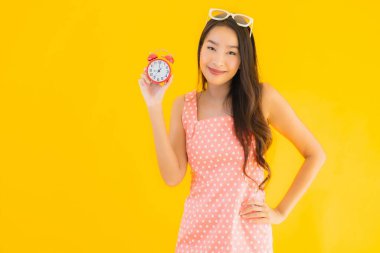 Güzel genç Asyalı kadın sarı izole arkaplanda alarm ya da saat gösteriyor.