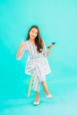 Güzel bir Asyalı kadın portresi akıllı cep telefonu kullanır ve mavi izole edilmiş arka planı olan bir sandalyeye oturur.