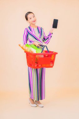 Marketten aldığı alışveriş sepetiyle güzel bir Asyalı kadının portresi. Renkli, izole arka plan.