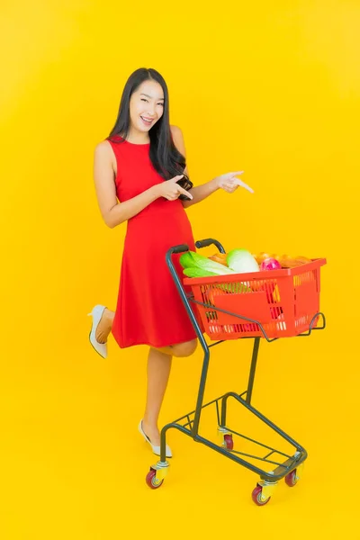 肖像画美しい若いアジアの女性は黄色の色の背景にスーパーマーケットから食料品バスケットと笑顔 — ストック写真