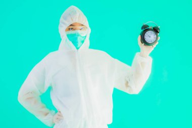 Güzel bir portre genç Asyalı doktor. Özel süit ve maske takıyor. Mavi arka planda saati ya da alarmı gösteriyor.