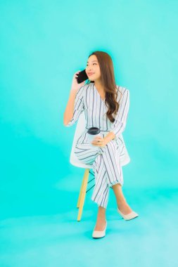 Güzel bir Asyalı kadın portresi akıllı cep telefonu kullanır ve mavi izole edilmiş arka planı olan bir sandalyeye oturur.