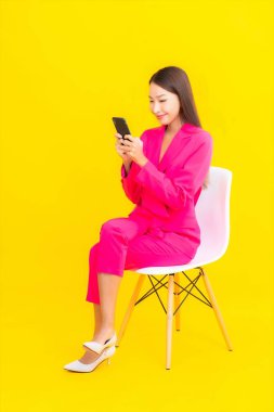 Güzel bir Asyalı kadın portresi sarı renkli izole edilmiş arka planda akıllı cep telefonu kullanır.