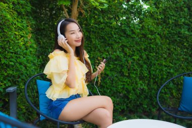 Genç Asyalı kadın kulaklıklı akıllı cep telefonunu açık hava bahçe manzaralı müzik için kullanıyor.