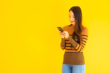 Güzel genç Asyalı kadın, sarı izole edilmiş arka planda birçok eylem içeren akıllı cep telefonu ya da cep telefonu kullanır.