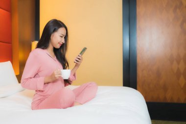 Güzel bir Asyalı kadın yatak odasının içinde akıllı cep telefonu kullanıyor.