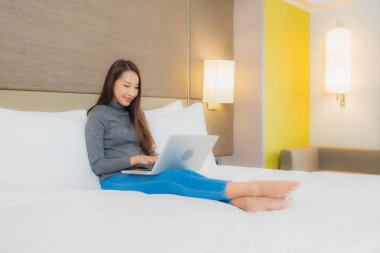 Güzel bir Asyalı kadın yatak odasının iç kısmında bilgisayar kullanıyor.