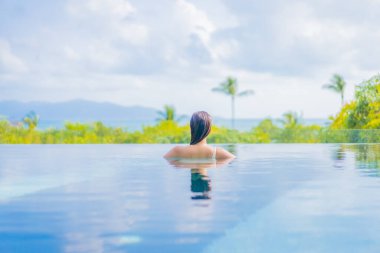 Güzel bir Asyalı kadın portresi gezide deniz manzaralı açık havuzda yüzüyor.