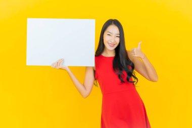 Asyalı güzel bir kadının portresi. Sarı arka planda boş beyaz ilan panosuyla gülümsüyor.