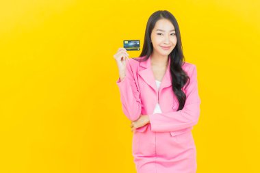 Asyalı güzel bir kadının portresi. Sarı arka planda kredi kartıyla gülümsüyor.