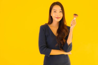 Sarı izole arkaplanda makyaj fırçası olan güzel bir Asyalı kadın portresi.