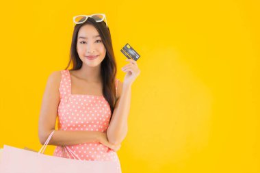 Renkli alışveriş çantalı güzel Asyalı kadın akıllı cep telefonu ve sarı izole edilmiş arka planda kredi kartı.